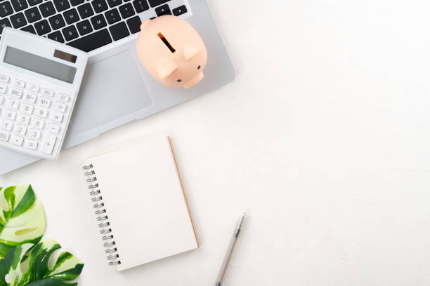 Dator, kalkylator, anteckningsblock, penna och spargris för att kartlägga ekonomin ligger på ett skrivbord